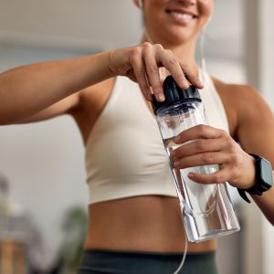 Close-up of thirsty female athlete opening water bottle at home.