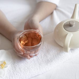 Female hands are holding a cup of tea, an orchid flower and a teapot, the concept of spa treatments and relaxation.